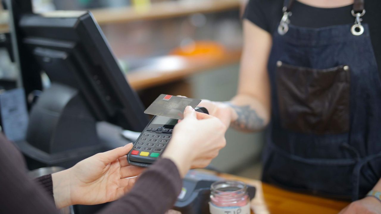 Close-up photo of a shop worker holding a debit card reader while a customer makes a payment