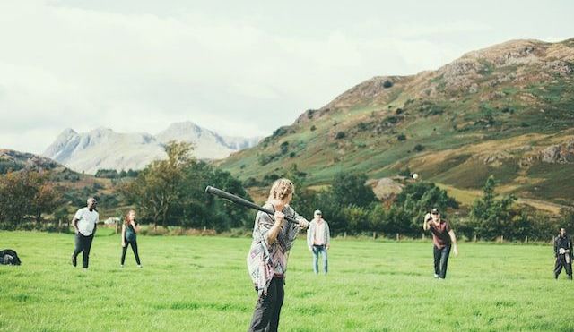 Group of people playing rounders outside on the grass with hills in the background