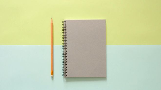 grey notebook next to a yellow, eraser-tipped pencil