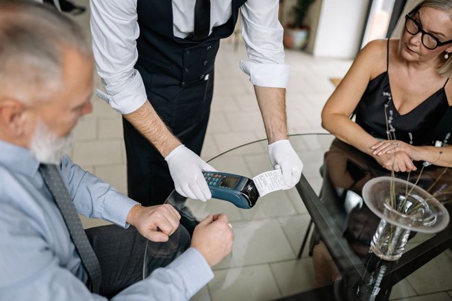 A man and woman sitting at a table in a restaurant, paying for a meal using a terminal