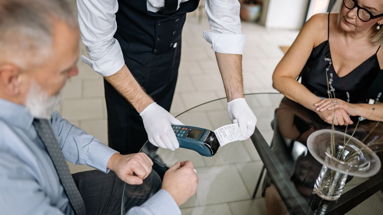 A man and woman sitting at a table in a restaurant, paying for a meal using a terminal