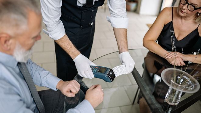 A man and woman sitting at a table in a restaurant, paying for a meal using a terminal
