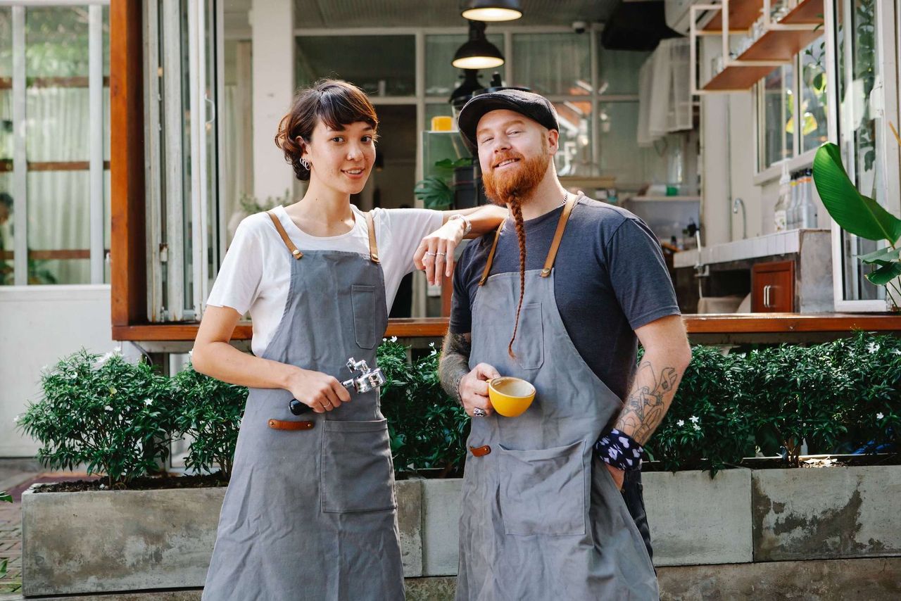 Female and male barista facing the camera and smiling in front of a shop