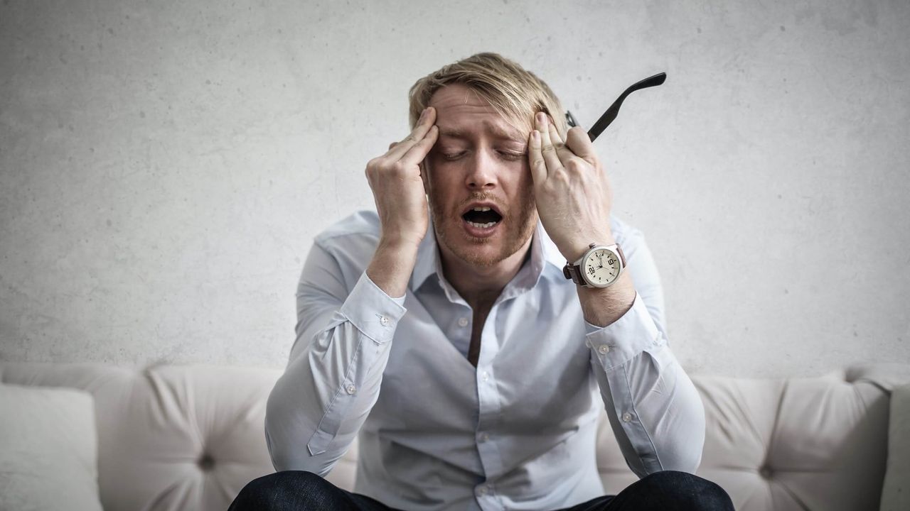 Man in business attire holding his classes and rubbing his temples.