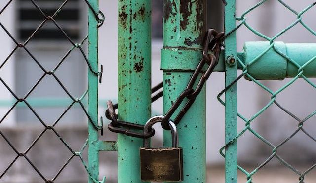 Rusted green metal gate locked shut with a chain and padlock