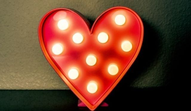 A red heart-shaped light box, leaning against a dark wall.