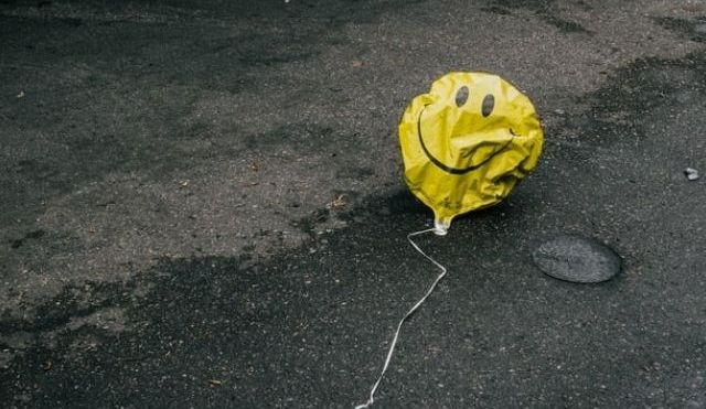 Deflated smiley face balloon, lying on the concrete