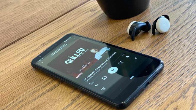 Phone on wooden table top with Grilled podcast on screen and earphones in the background