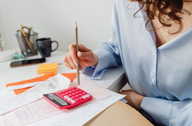 Female professional sitting at a desk covered with papers using a vivid pink calculator