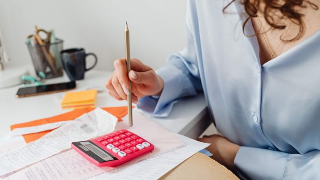 Female professional sitting at a desk covered with papers using a vivid pink calculator