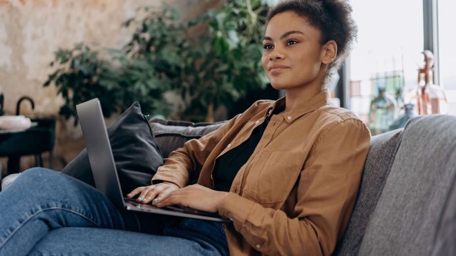 Women wearing jacket and jeans sitting on sofa using a laptop