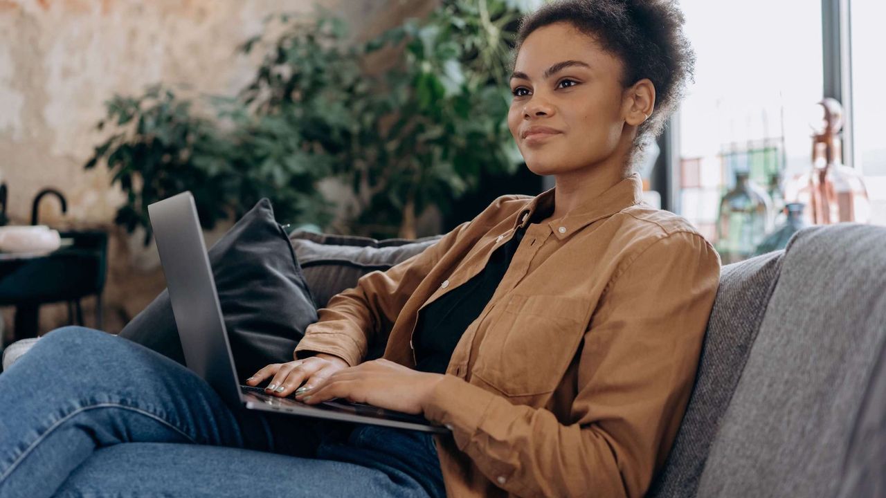 Women wearing jacket and jeans sitting on sofa using a laptop