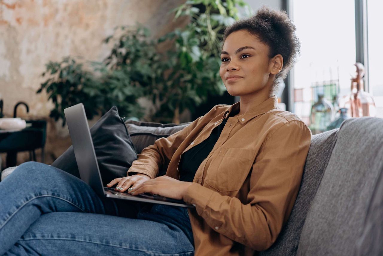 Women wearing jacket and jeans sitting on sofa using a laptop