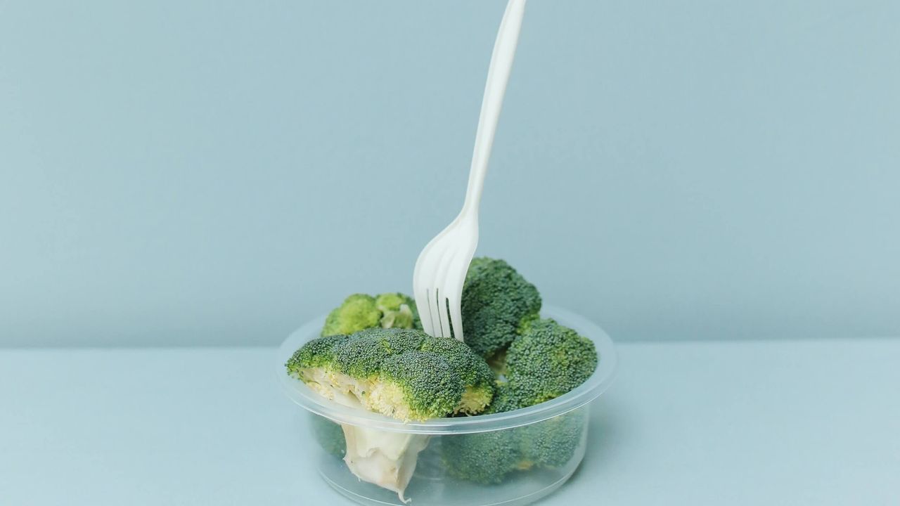 A clear plastic container filled with broccoli with a white plastic fork sticking out of it.