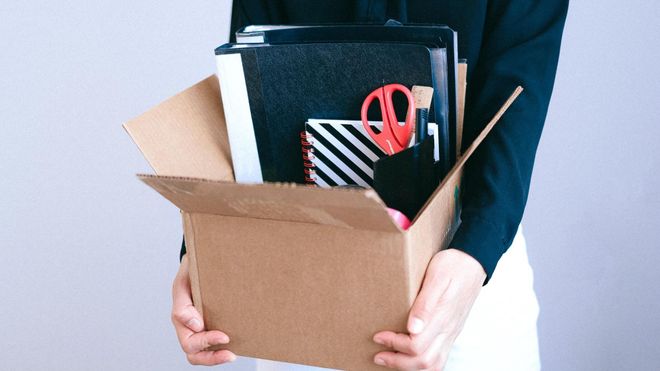 Close up photo of a woman holding a cardboard box filled with stationery items,