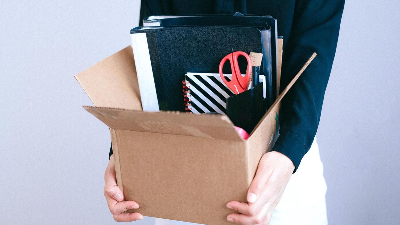 Close up photo of a woman holding a cardboard box filled with stationery items,