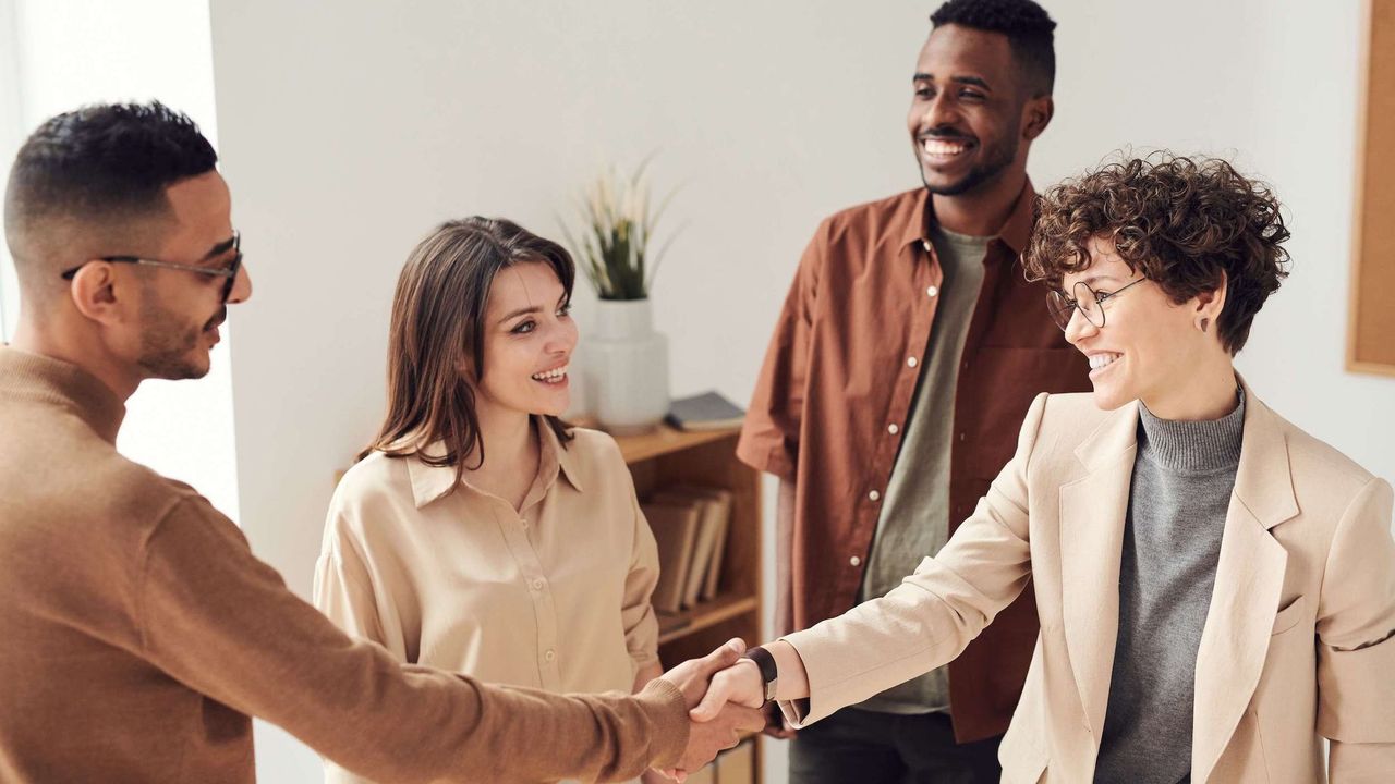 Woman with curly hair shaking hands with man wearing glasses as two other people look on, smiling.