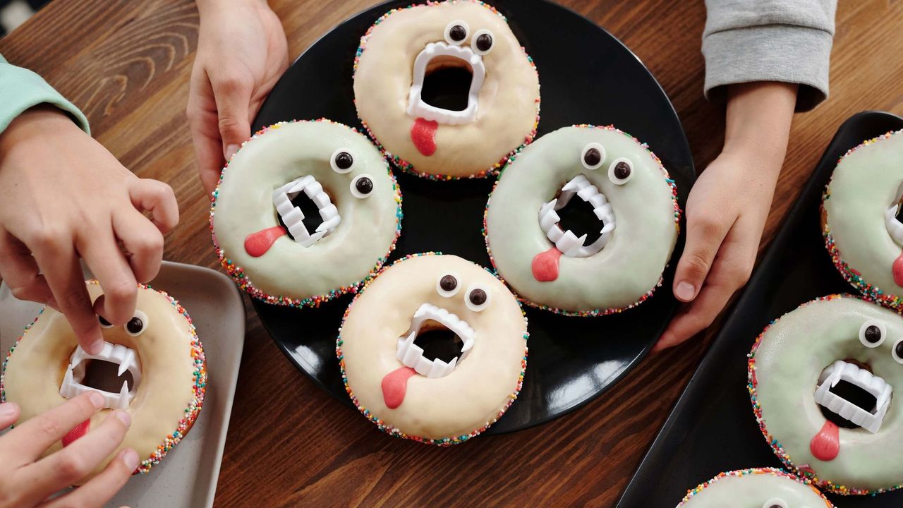 Close up of plates of Halloween-themed doughnuts with false vampire teeth being prepared by children's hands.