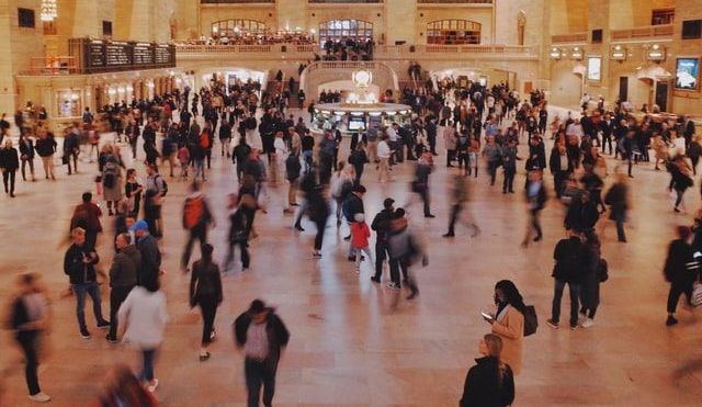 Many people walking across a busy station concourse, some figures blurred due to movement