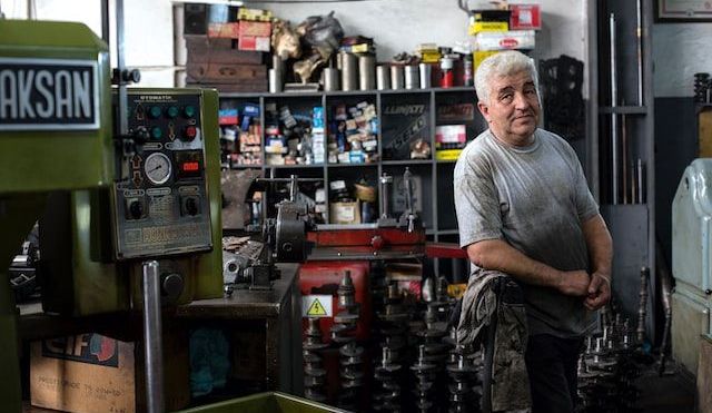 Man looking sidelong at the camera from inside his mechanic business