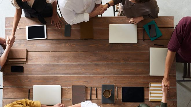 Top-down photo of coworkers around a rectangular wooden table shaking hands
