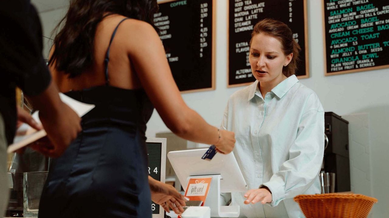 A woman in a dark blue dress paying in a cafe using her credit card.