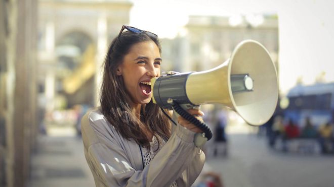 Photo of a young woman smiling while speaking into a large megaphone