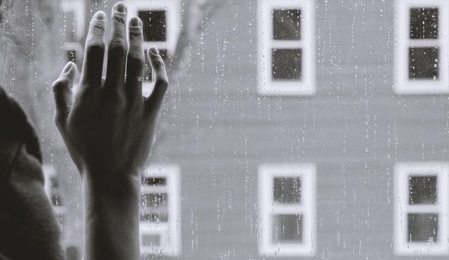 Woman's hand against a window pane, rain on the glass and a building opposite