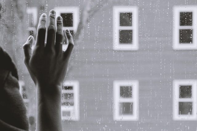 Woman's hand against a window pane, rain on the glass and a building opposite