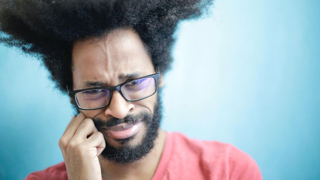 Man with glasses cringing while looking at the camera.
