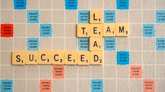 A Scrabble game board with the words 'lead', 'team' and 'succeed' spelled out in beige Scrabble tiles.