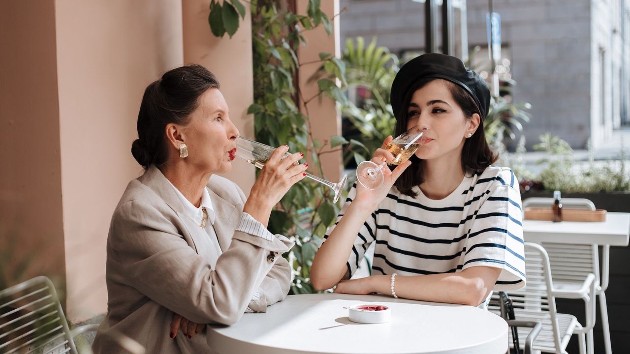 Mother and daughter sipping champagne at at outdoor cafe table