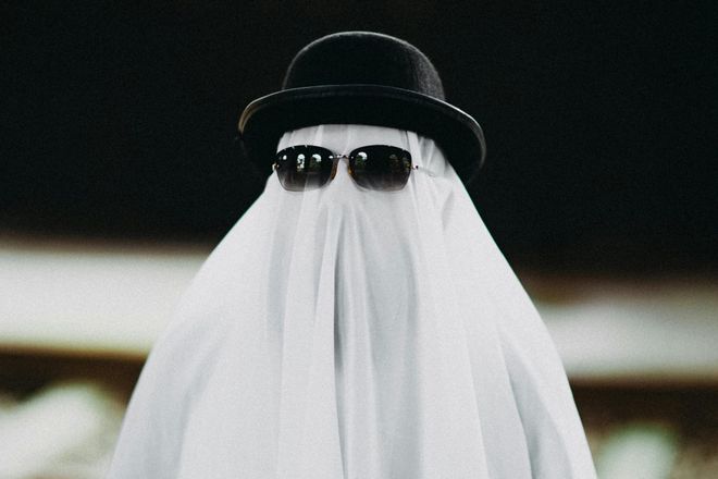 Someone covered in a white sheet to look like a ghost, with sunglasses and a bowler hat over the sheet.