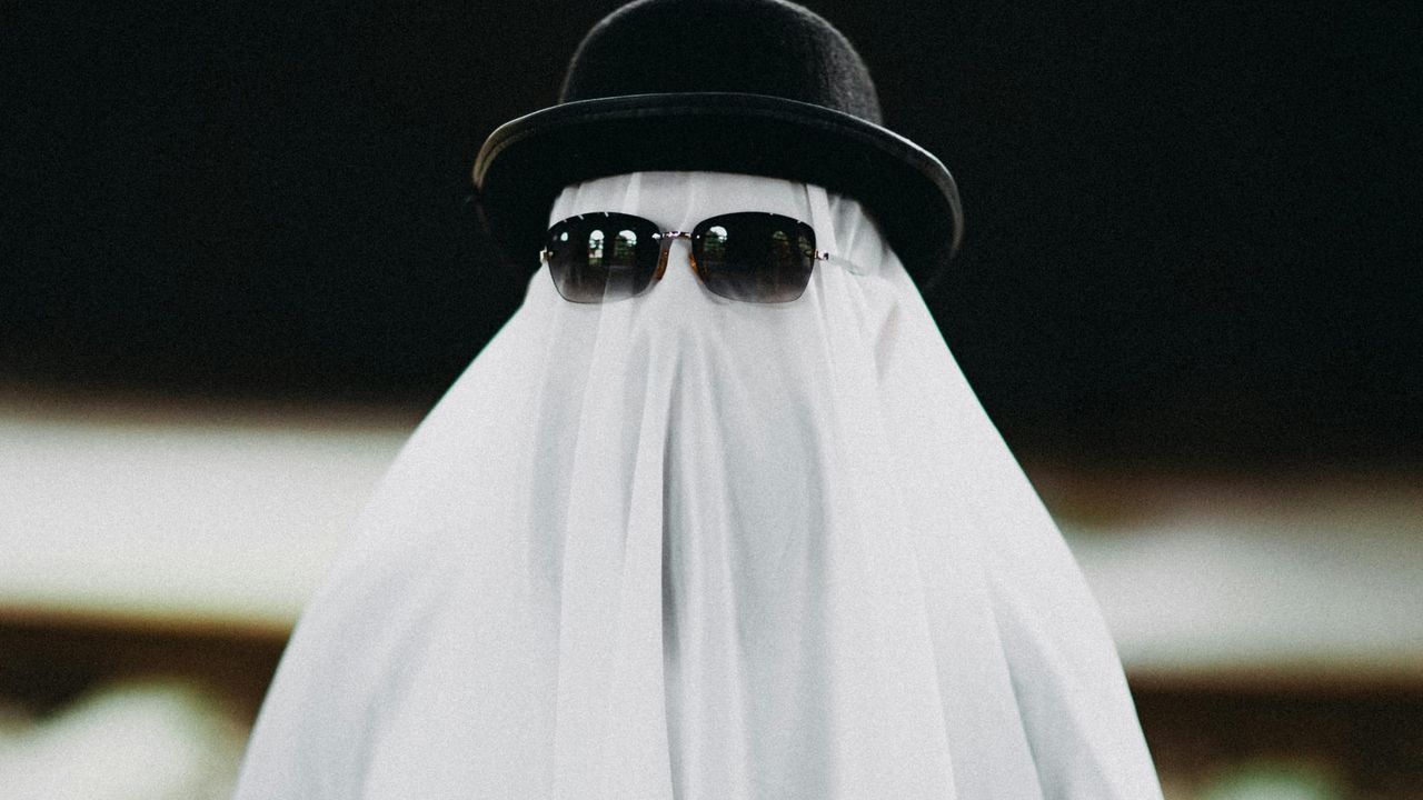 Someone covered in a white sheet to look like a ghost, with sunglasses and a bowler hat over the sheet.