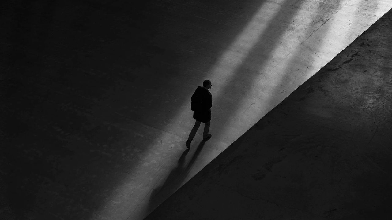 A black and white image, showing a distant silhouette of someone walking away.