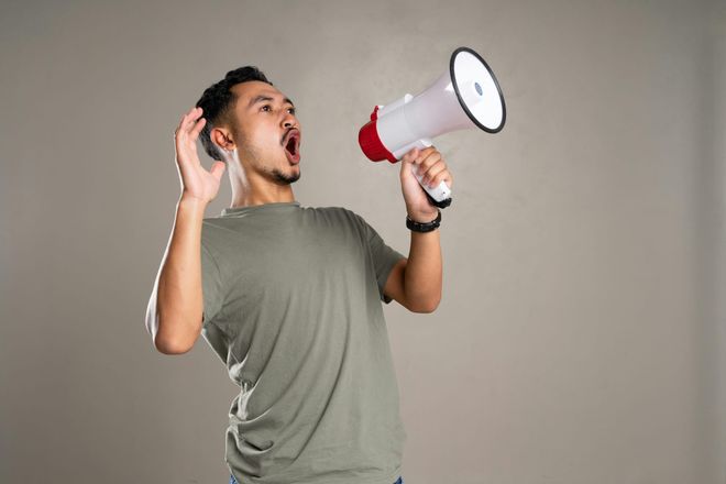 A man in a grey t-shirt leaning back and yelling into a megaphone.