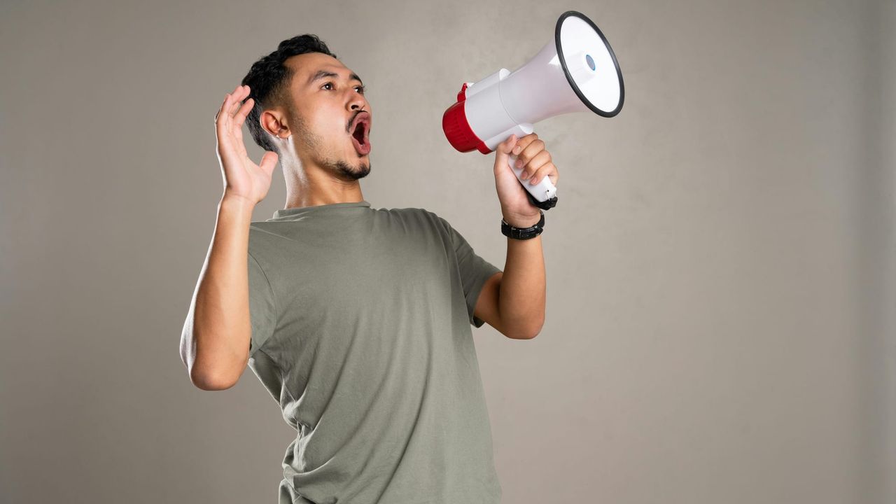 A man in a grey t-shirt leaning back and yelling into a megaphone.