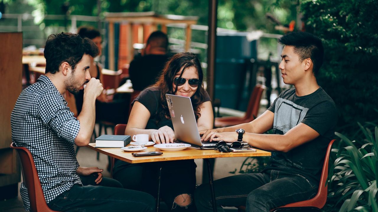 Two men and a woman sitting at an outside table having an informal meeting and drinking coffee