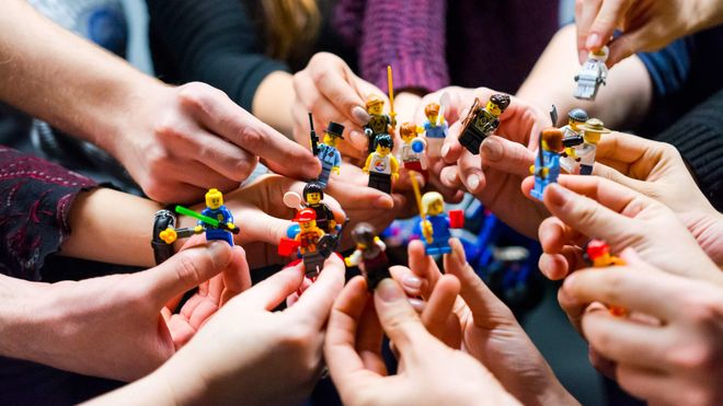 Many hands holding tiny Lego figures in a variety of outfits and holding different tools.