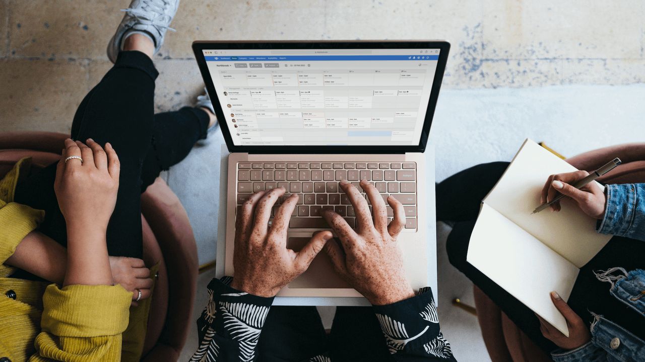 Top-down view of a person with an open laptop computer on their lap as two people sit either side of them.
