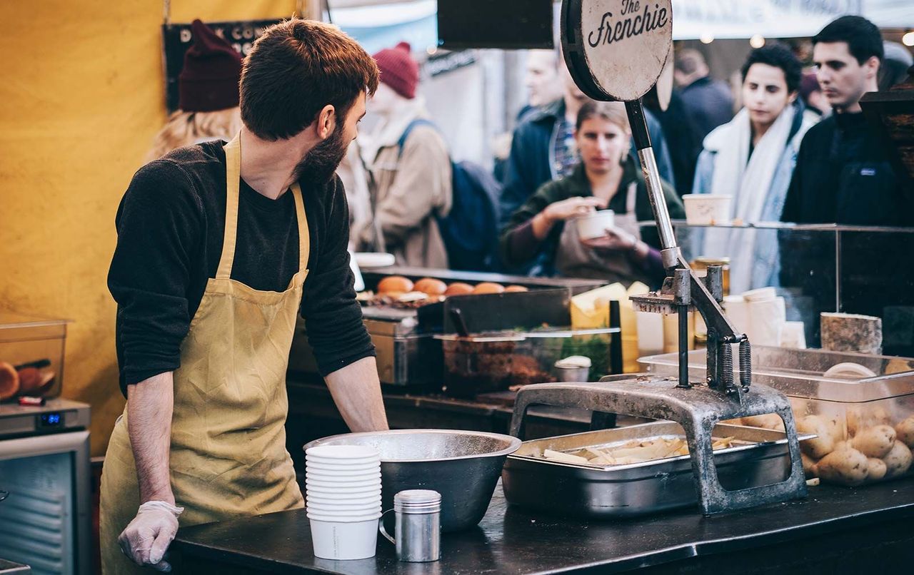 Food stall owner wearing an apron, looking over his shoulder at patrons.