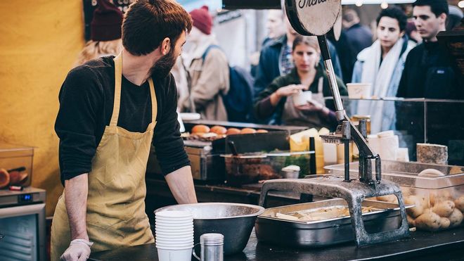 Food stall owner wearing an apron, looking over his shoulder at patrons.