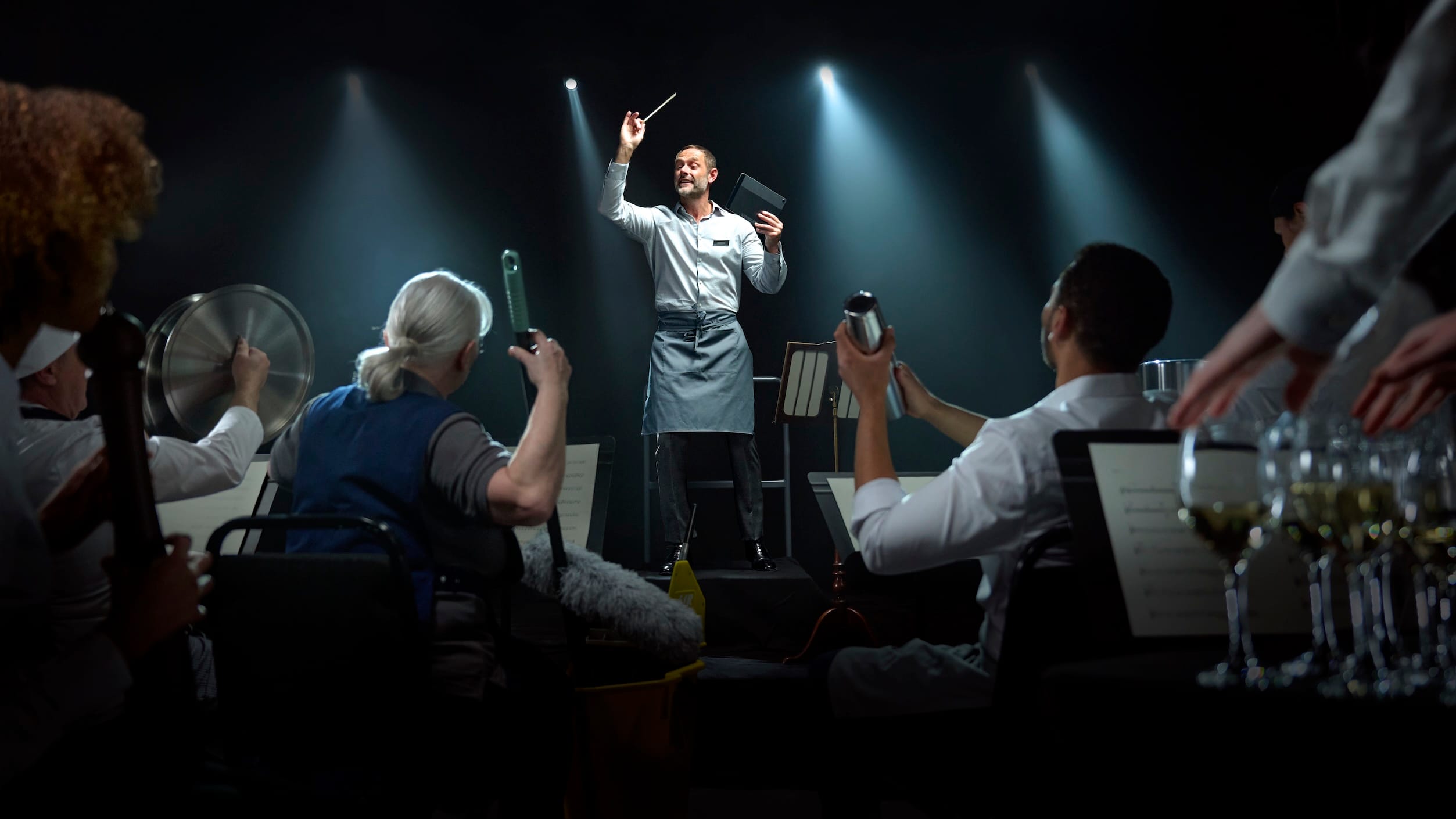 A man dressed as a waiter conducting an orchestra of hospitality staff