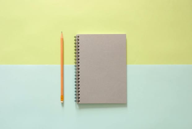 grey notebook next to a yellow, eraser-tipped pencil