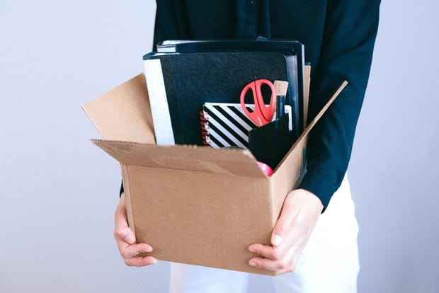 Close up photo of a woman holding a cardboard box filled with stationery items,