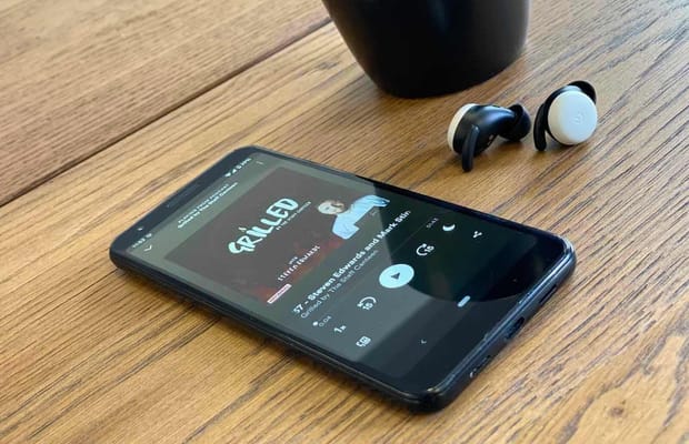 Phone on wooden table top with Grilled podcast on screen and earphones in the background