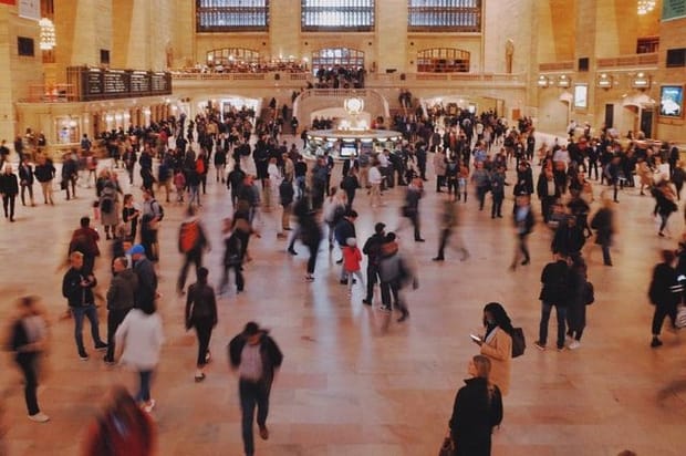 Many people walking across a busy station concourse, some figures blurred due to movement