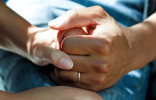 Close-up photo of hands holding, one of which is wearing a wedding ring.