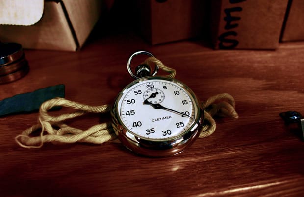 A gold stopwatch with white face on a wooden desk.