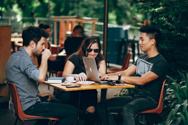 Two men and a woman sitting at an outside table having an informal meeting and drinking coffee